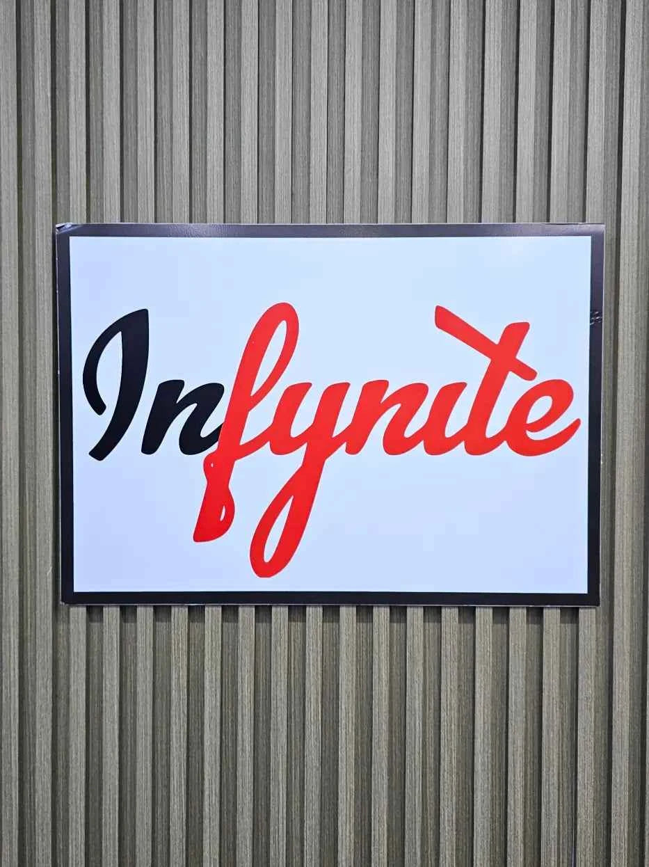 Infynite logo on a rectangular sign with a white background against a corrugated metal wall.