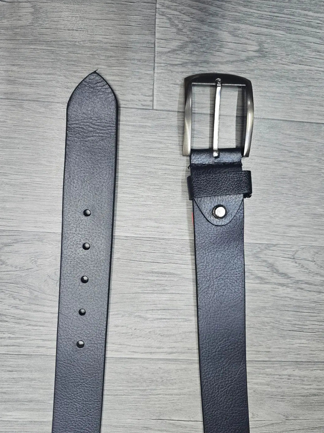 Black leather belt with silver buckle on a gray wooden surface