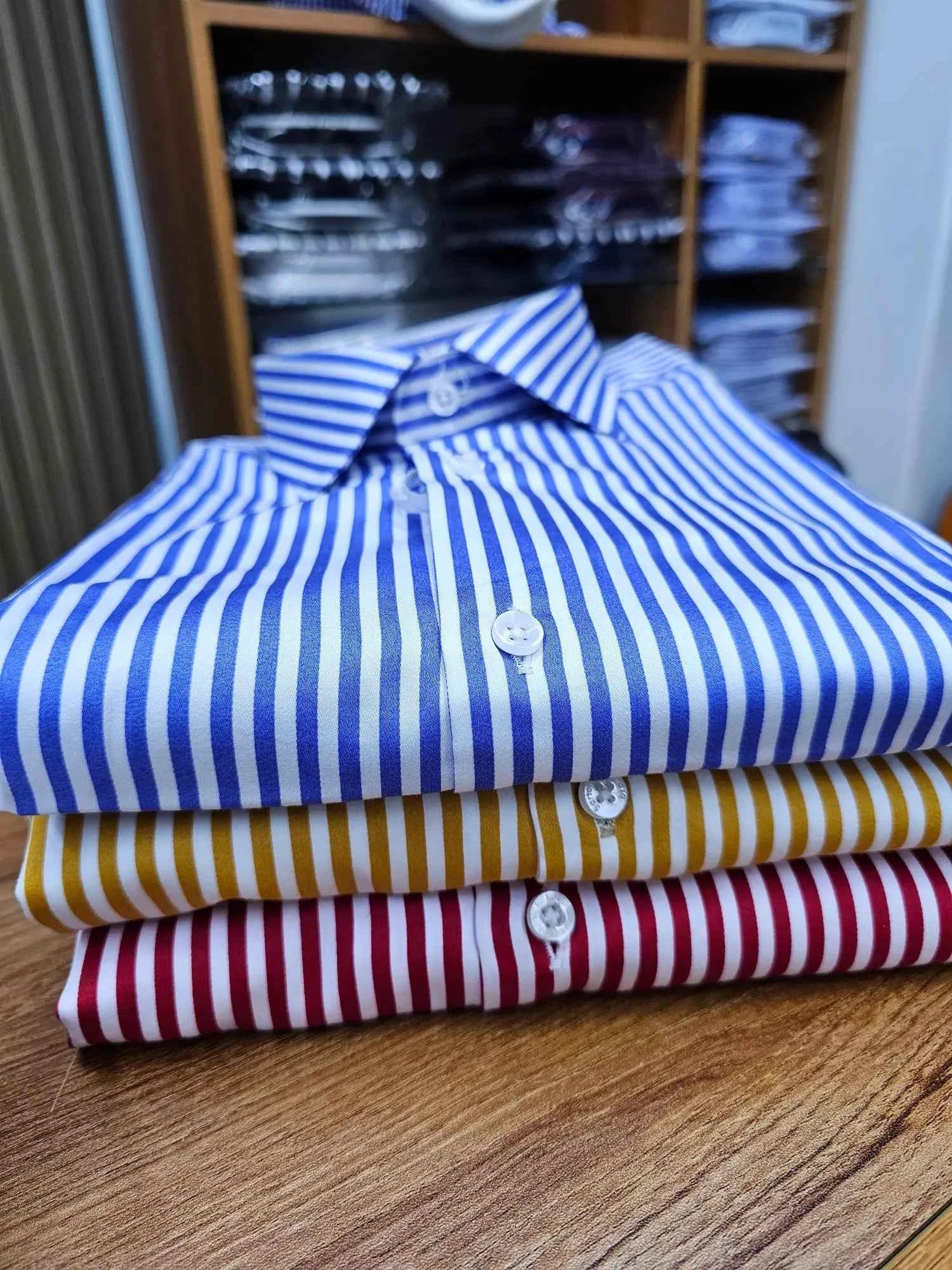 Stack of folded striped shirts in blue, yellow, and red on a wooden surface with a blurred background.