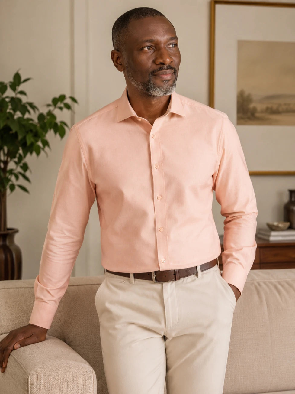 Man wearing a light pink shirt and beige pants in a living room setting.