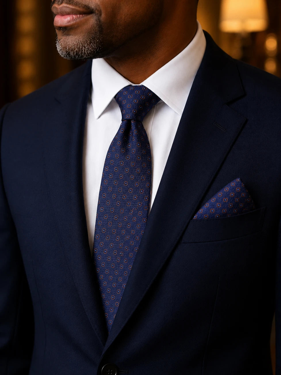 Man wearing a navy suit with a patterned tie and pocket square.