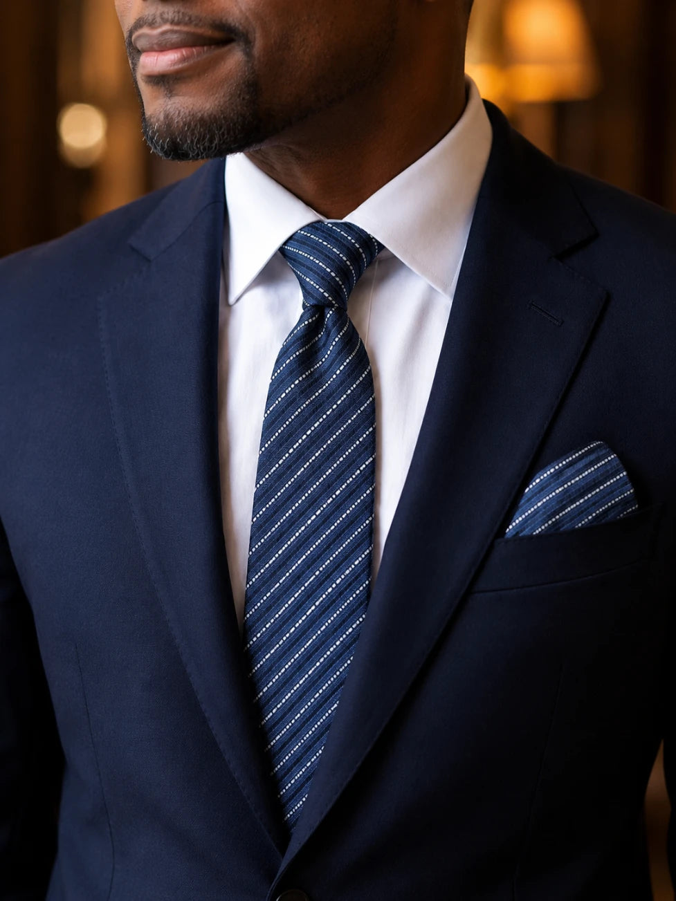 Man wearing a navy suit with a striped tie and pocket square.