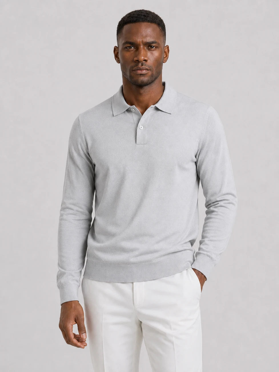 African man wearing an Infynite light grey long-sleeve knitted polo sweater with off-white trousers.
