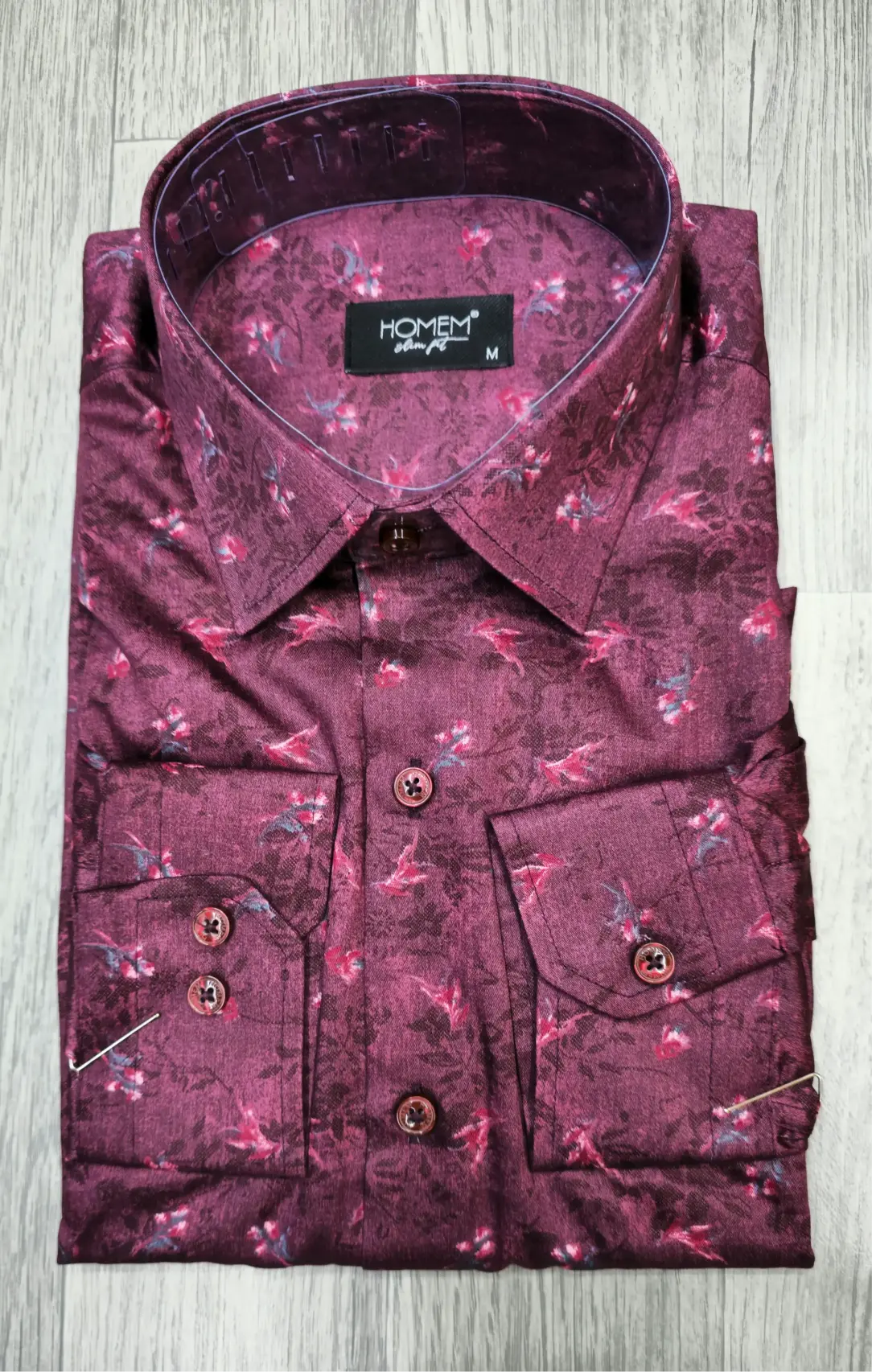 Folded maroon floral shirt with a brand label on a light wooden surface