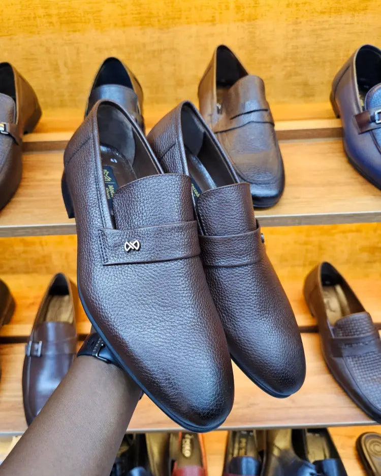 Brown leather shoes with a metallic buckle held by a hand against a wooden background.