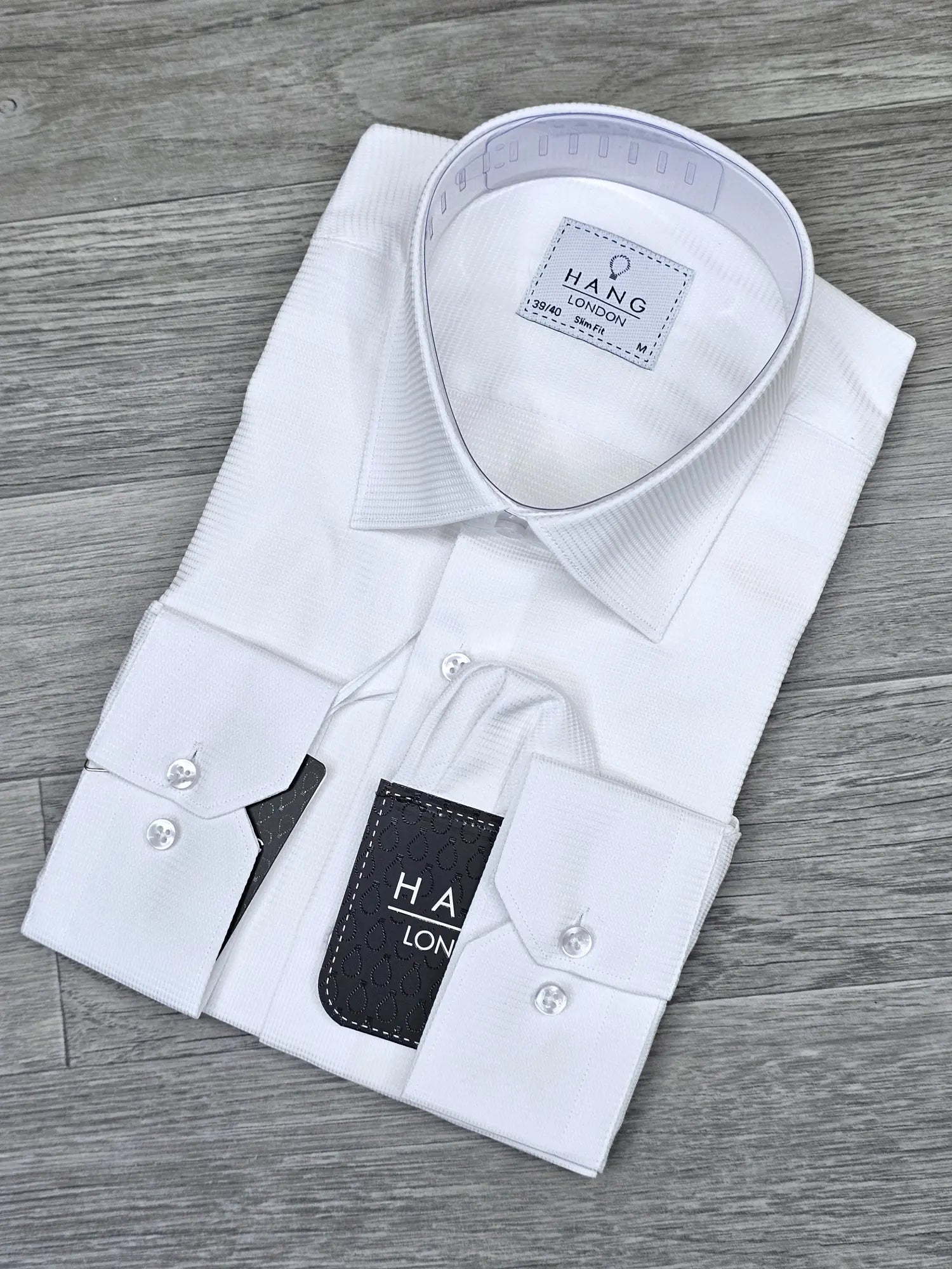 Folded white dress shirt with 'HANG London' label on a wooden surface