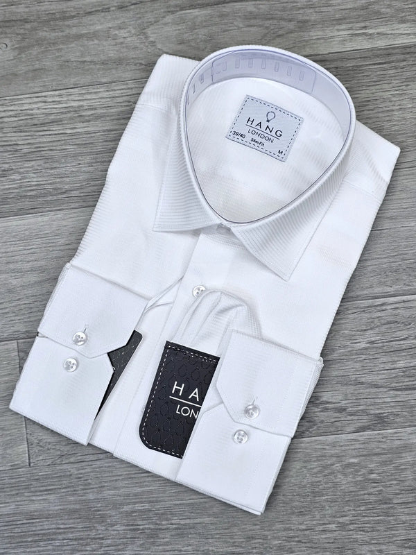 Folded white dress shirt with 'HANG London' label on a wooden surface