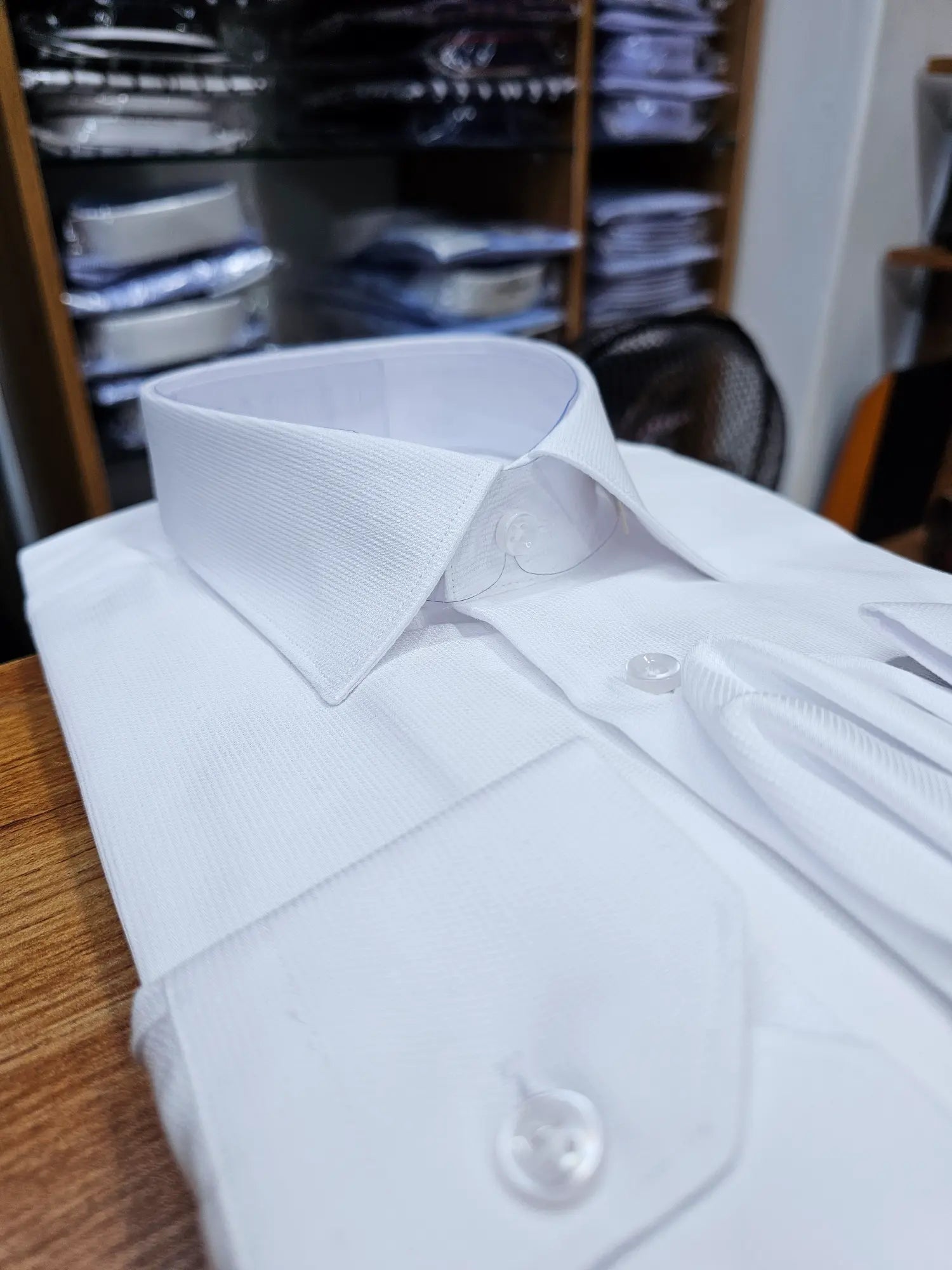 White dress shirt on a wooden surface with a blurred background of shelves.