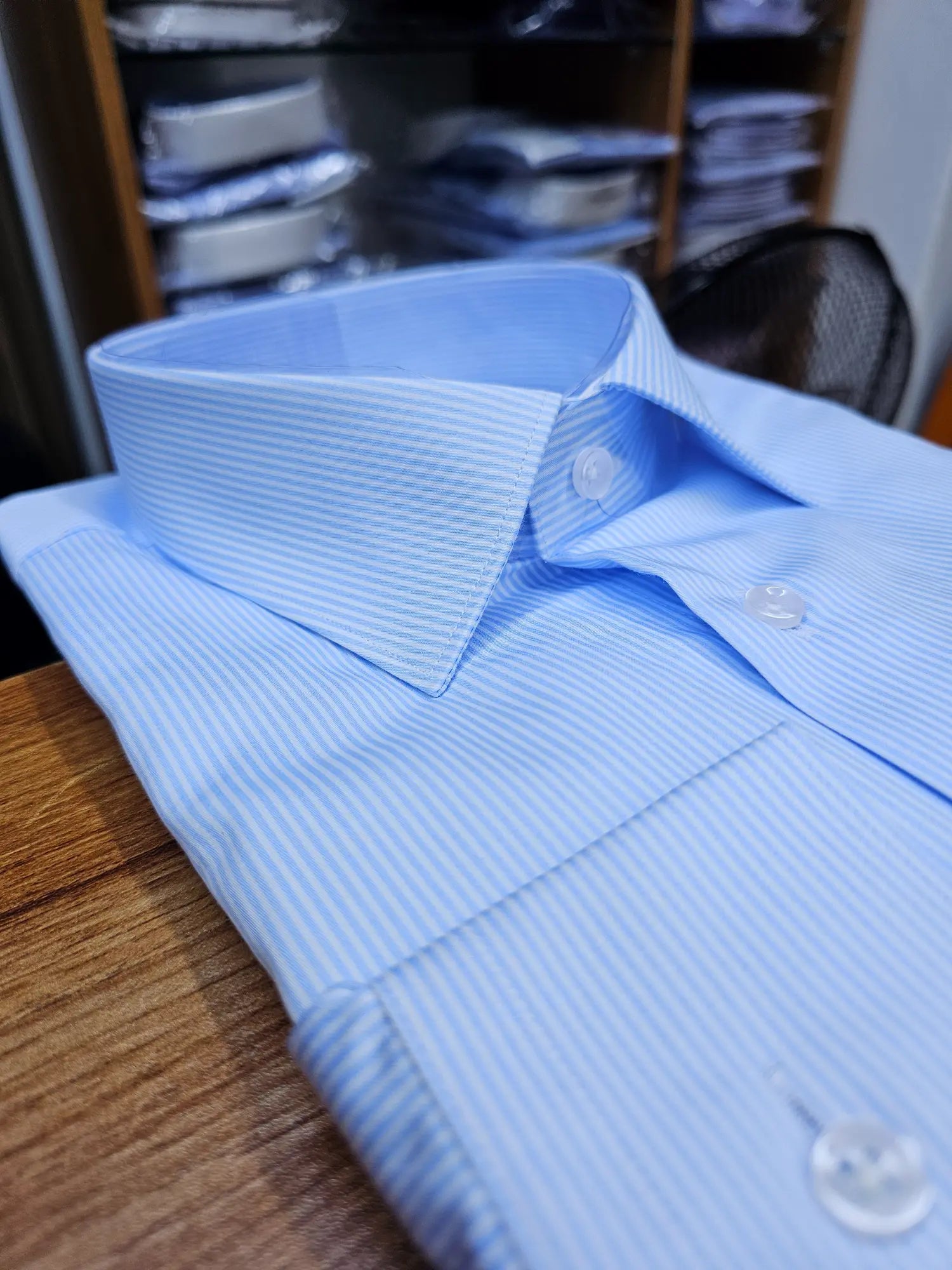Folded light blue dress shirt on a wooden surface with a blurred background