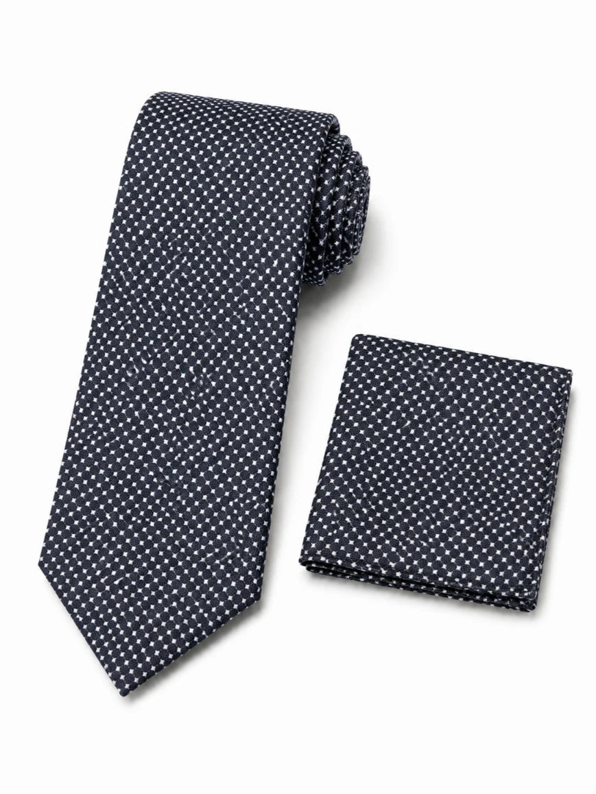 Infynite charcoal black micro cross-dot tie and pocket square set with white X-shaped dots on woven textured base laid flat on white background