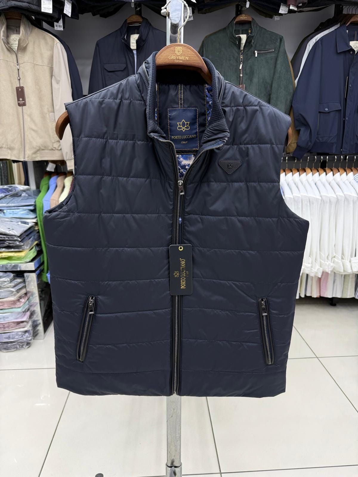 Navy puffer vest on a rack with clothing in the background