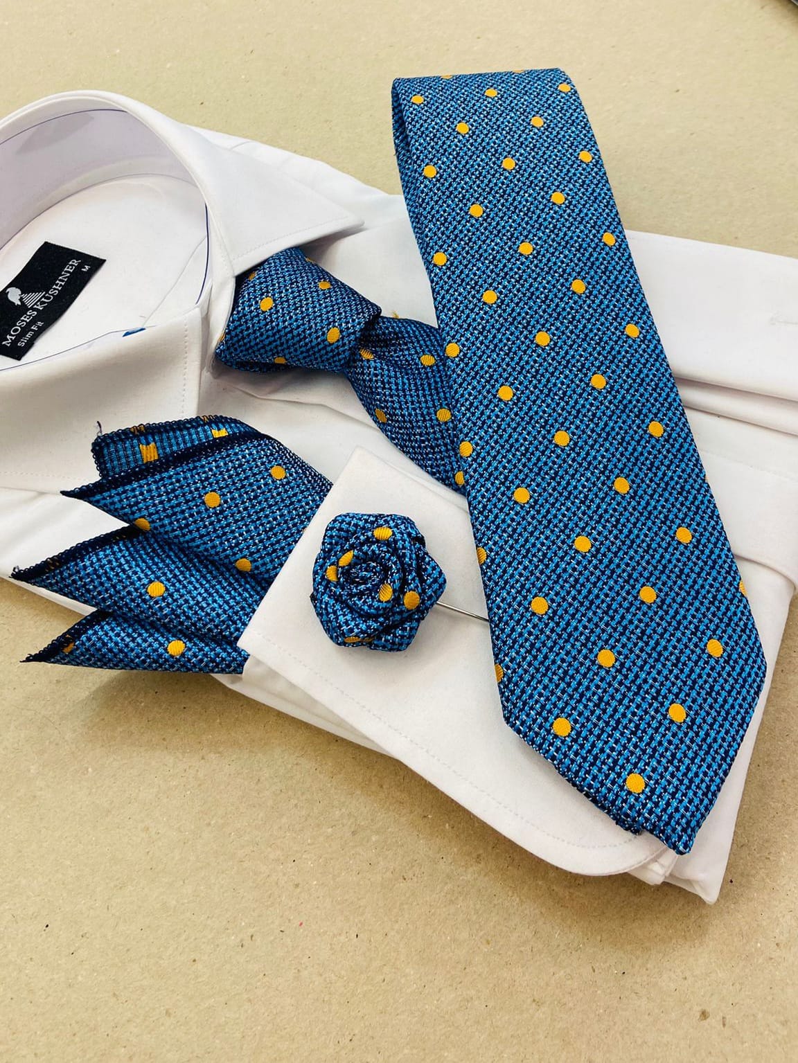 Blue tie with yellow dots, pocket square, and cufflinks on a white shirt with visible brand label.