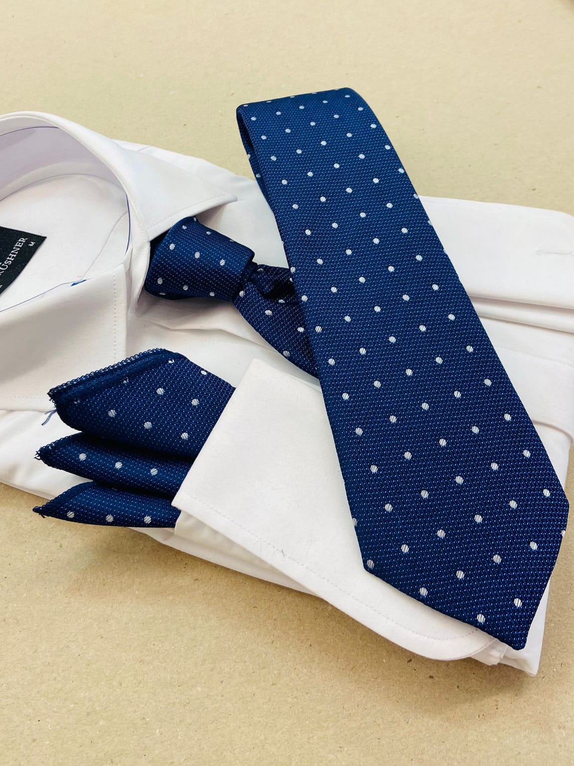 Blue polka dot tie and cufflinks on a white shirt with a beige background