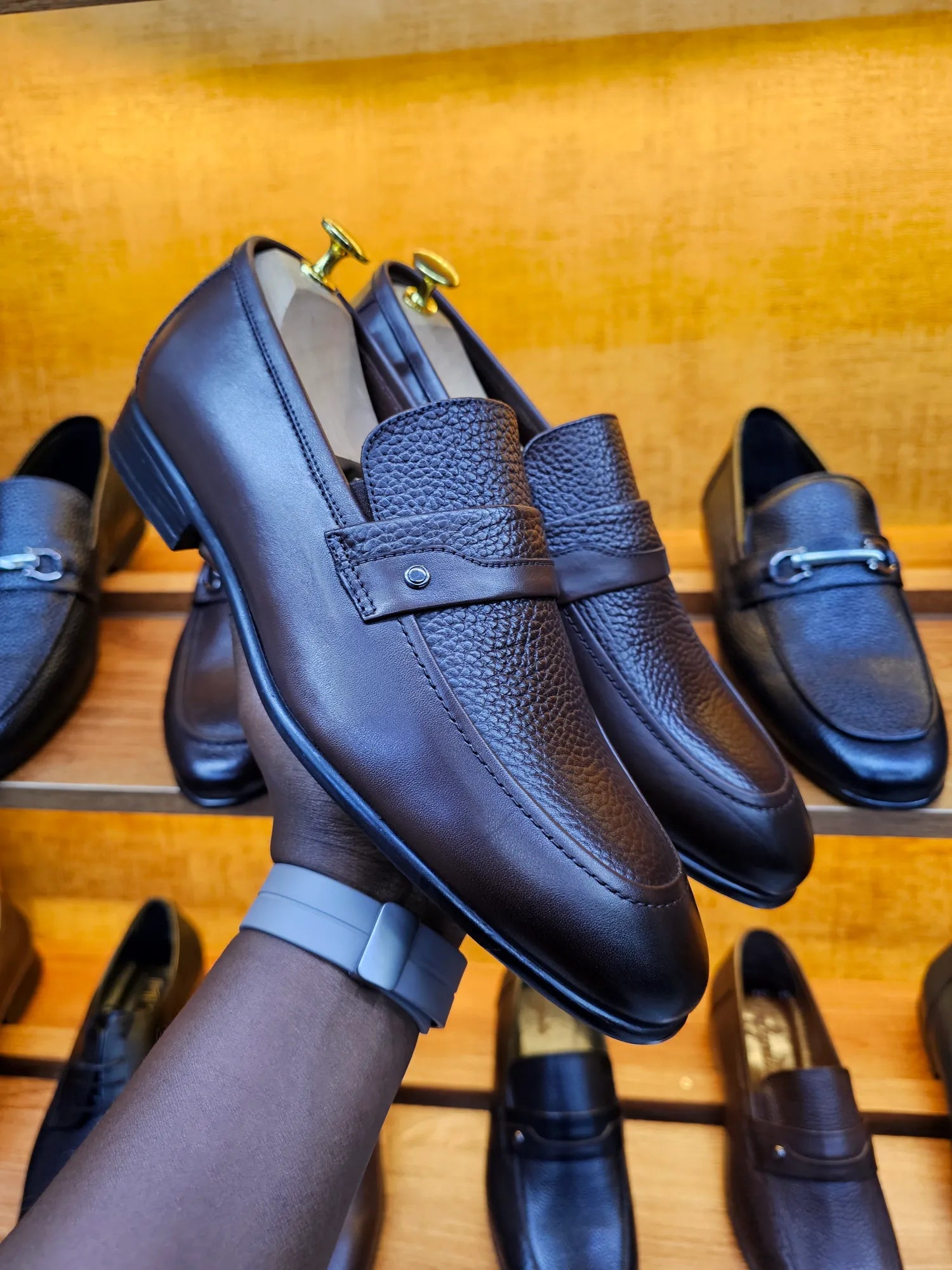 Black leather loafers held by a hand against a wooden background