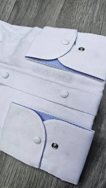 White dress shirt sleeves with snap-button cuffs and a blue textured inner lining, laid flat on a gray wood surface.