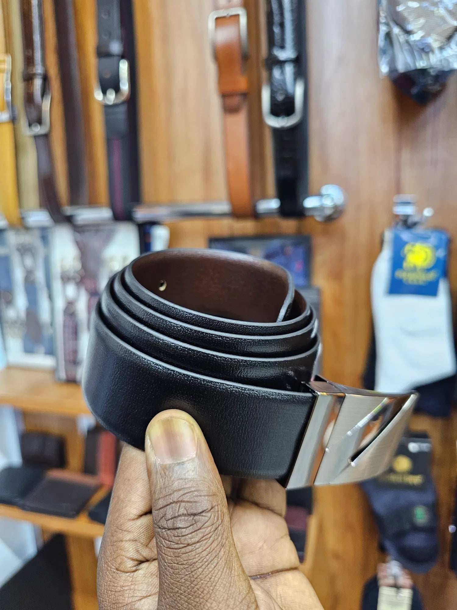 Stack of black leather belts held by a hand with a blurred background of more belts.