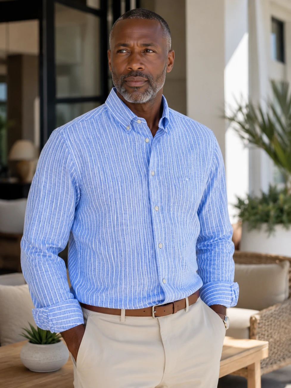 Man wearing a blue striped shirt and beige pants standing outdoors.