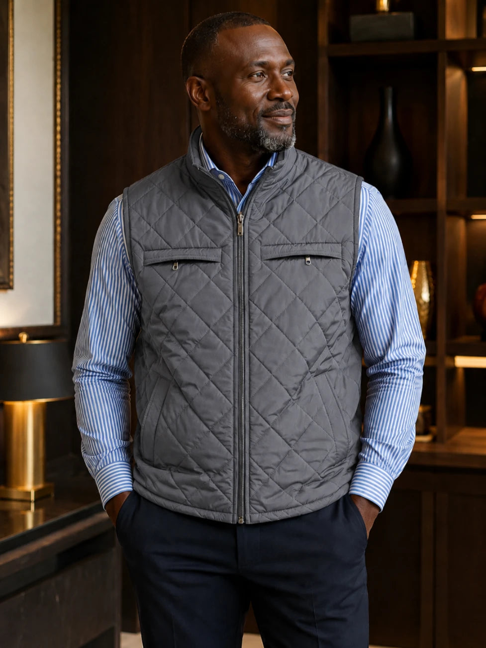Man wearing a green quilted vest over a blue striped shirt in an indoor setting.