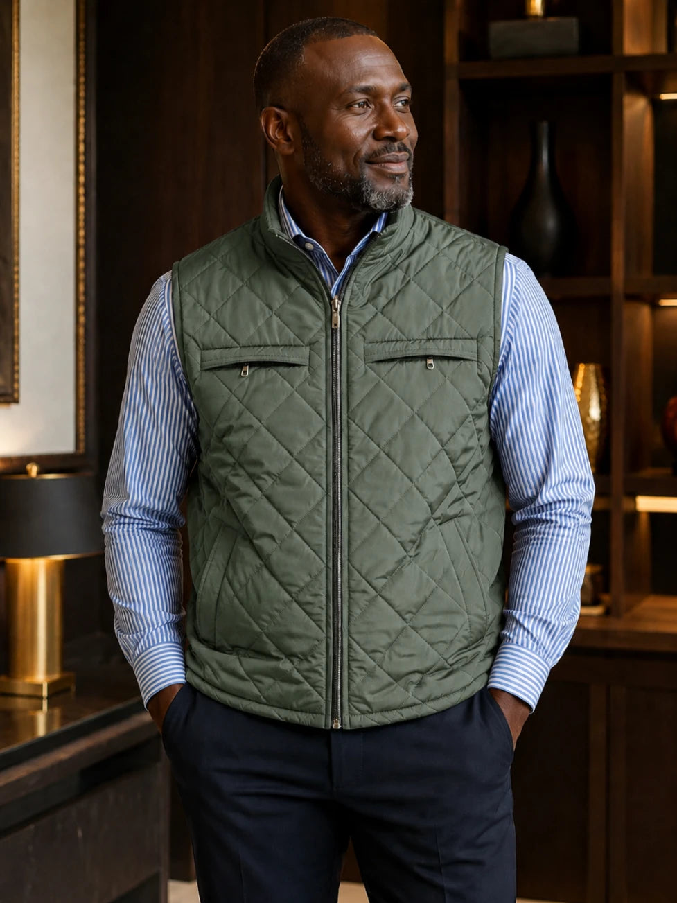 Man wearing a green quilted vest over a blue striped shirt in an indoor setting.