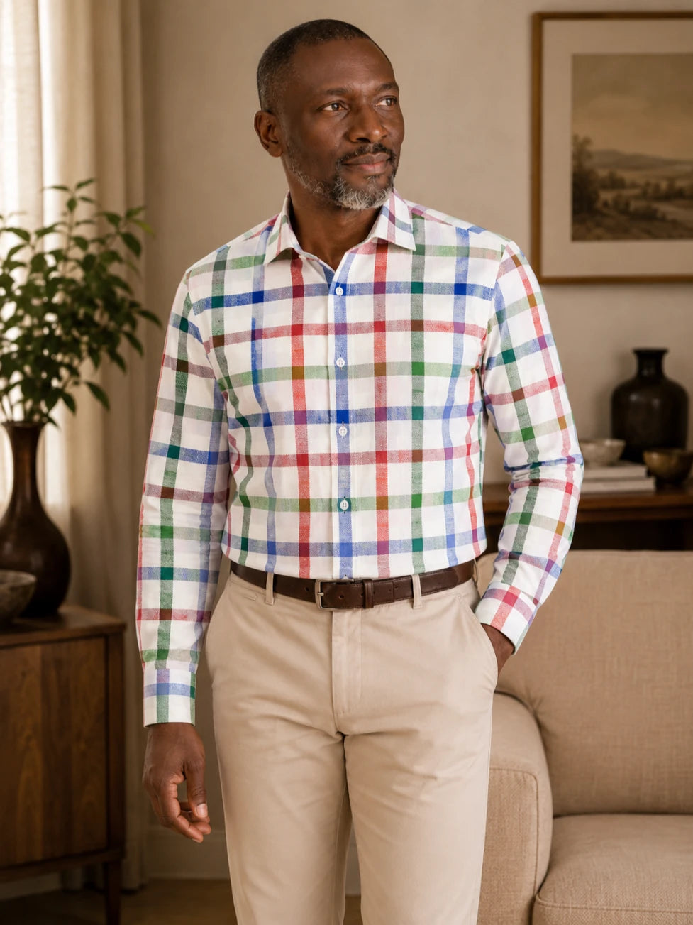 Man wearing a multicolored checkered shirt and beige pants in a living room setting.