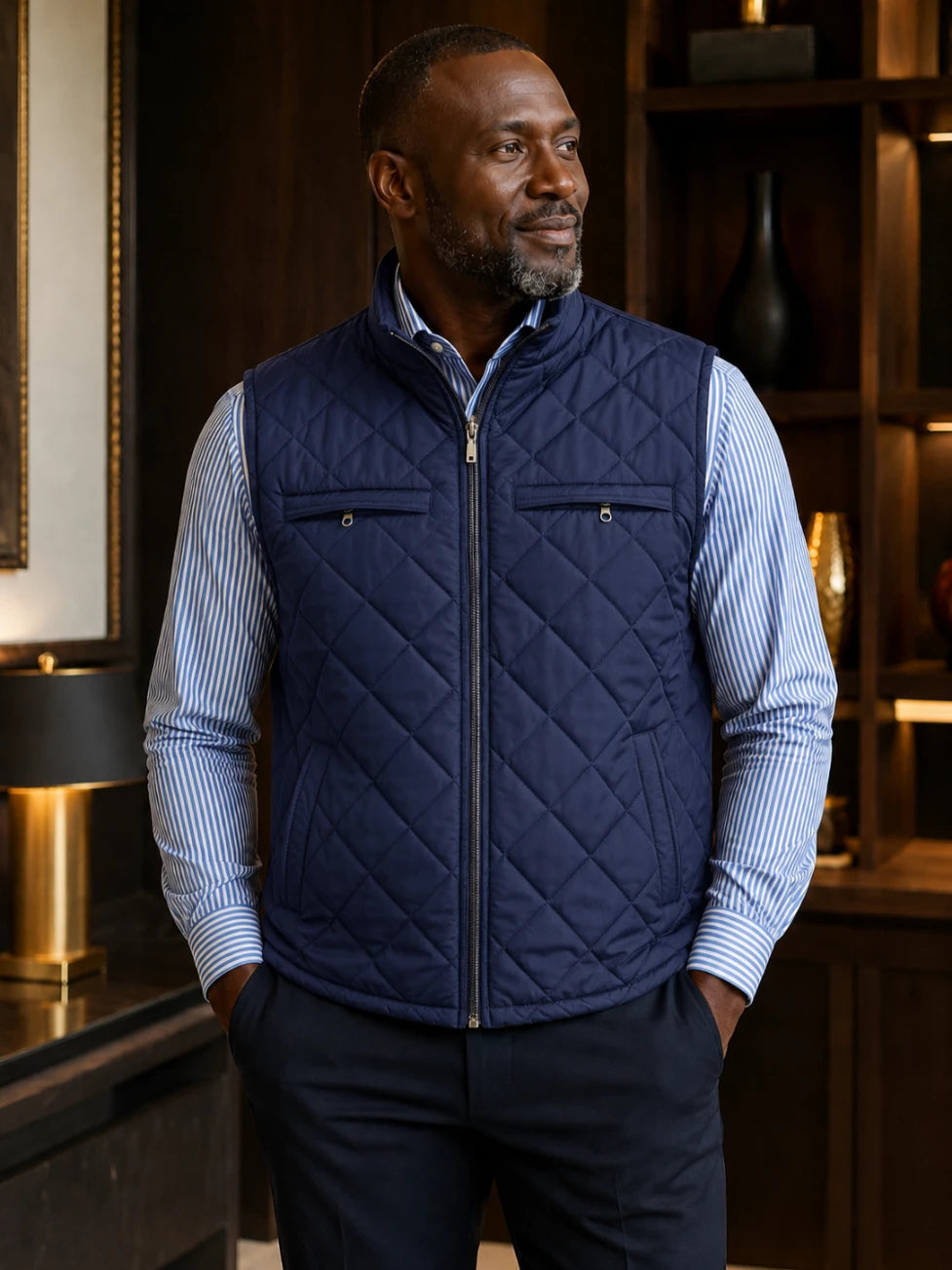 Man wearing a navy quilted vest over a striped shirt in an indoor setting.