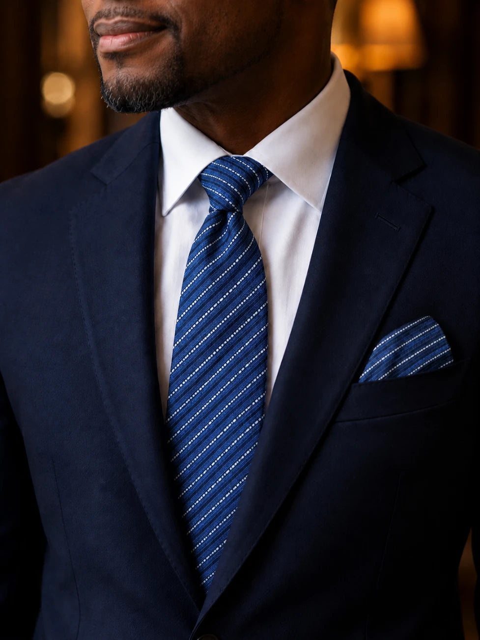 Man wearing a navy suit with a blue striped tie and pocket square.