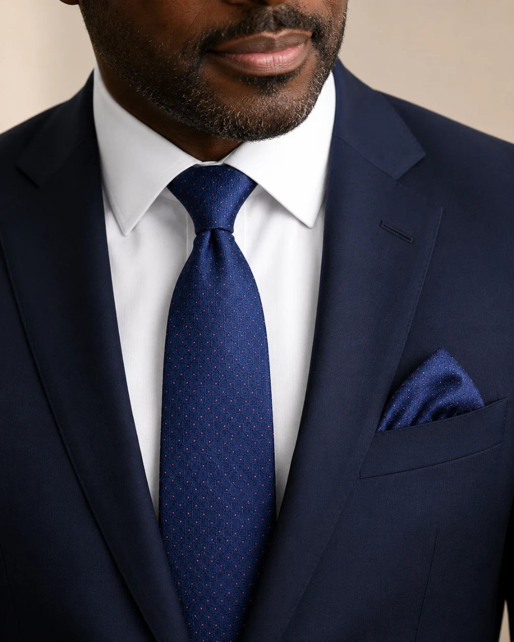 Man wearing a navy suit with a matching tie and pocket square.