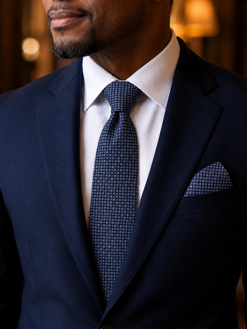 Man wearing a navy suit with a patterned tie and pocket square.
