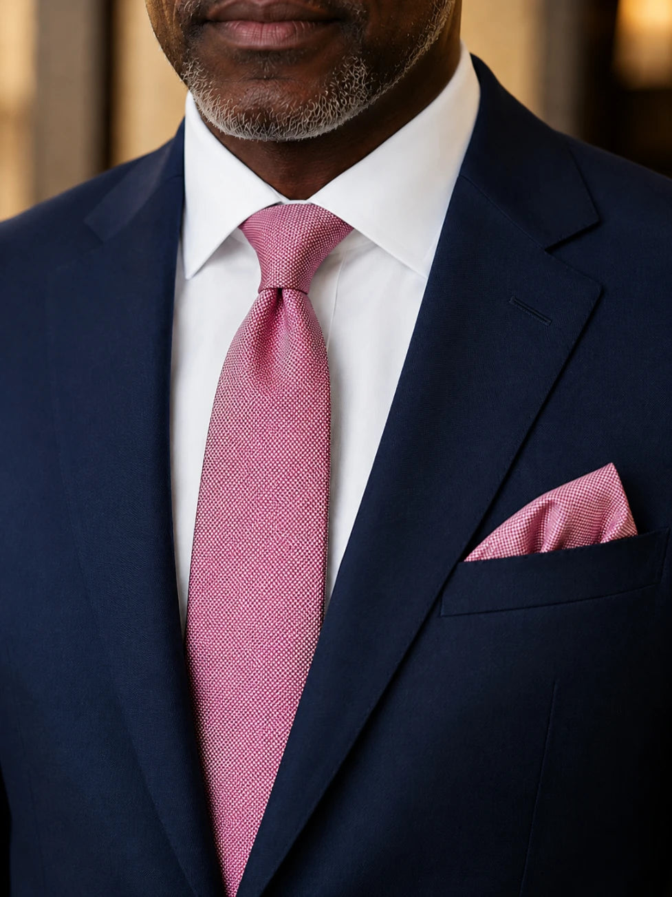Man wearing a navy suit with a pink tie and pocket square.
