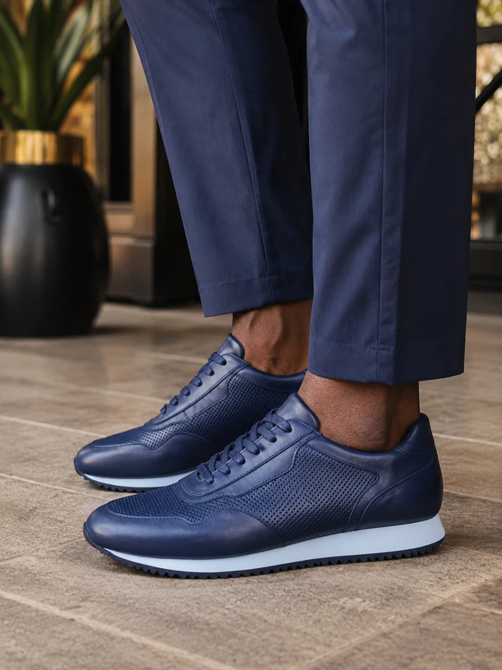 Navy blue sneakers worn with dark pants on a tiled floor.