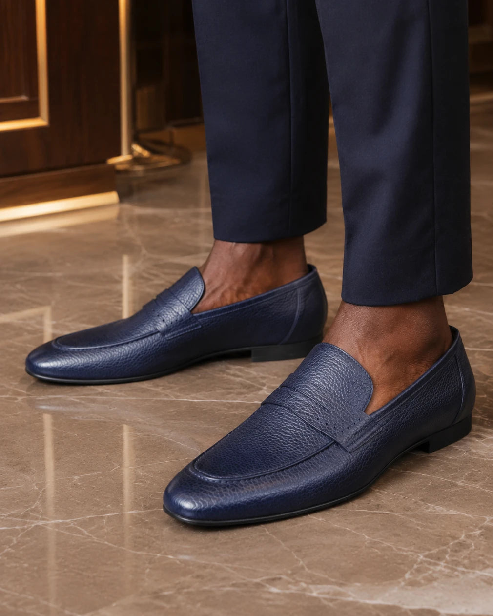 Navy loafers worn with dark pants on a marble floor